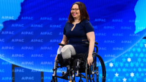 Tammy Duckworth on stage smiling with the AIPAC logo behind her.