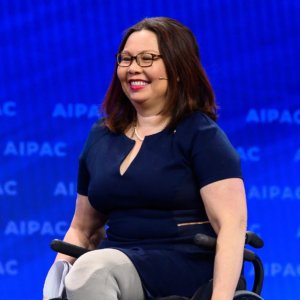 Tammy Duckworth on stage smiling with the AIPAC logo behind her.