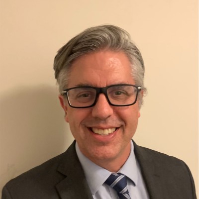 Craig Leen smiling headshot wearing glasses and a suit and tie