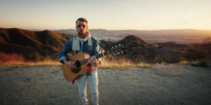 Charlie Kramer playing guitar in front of mountains in a scene from his music video