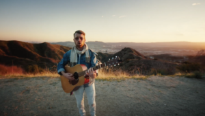 Charlie Kramer playing guitar in front of mountains in a scene from his music video