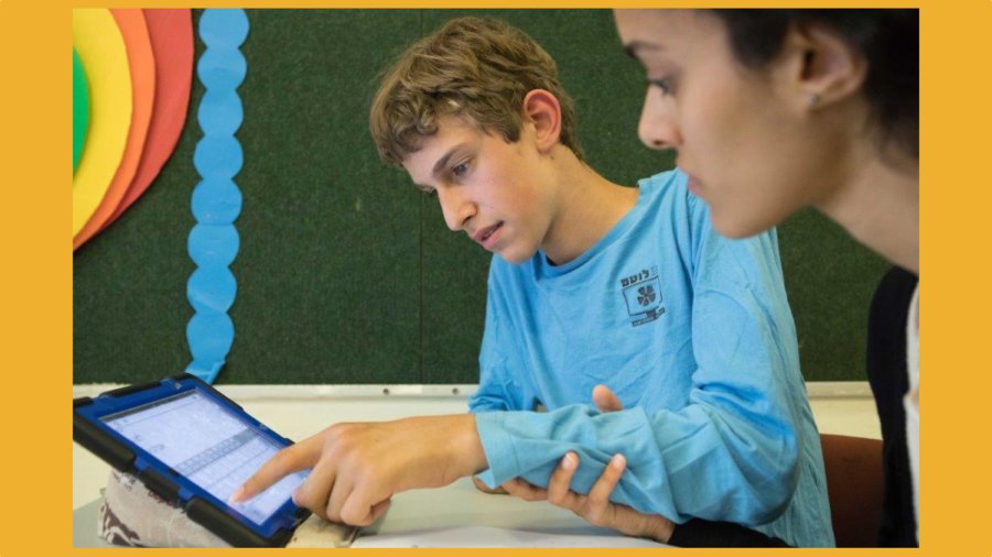 A boy with a disability and a teacher use an iPad together in a classroom