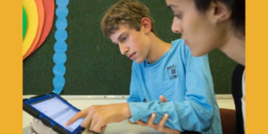 A boy with a disability and a teacher use an iPad together in a classroom