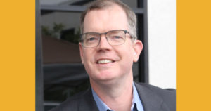 Delbert Whetter smiling headshot wearing glasses and a suitjacket