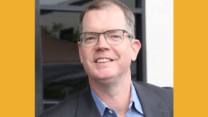 Delbert Whetter smiling headshot wearing glasses and a suitjacket