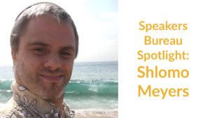 Shlomo Meyers smiling headshot on the beach with the ocean behind him. Text: Speakers Bureau Spotlight: Shlomo Meyers