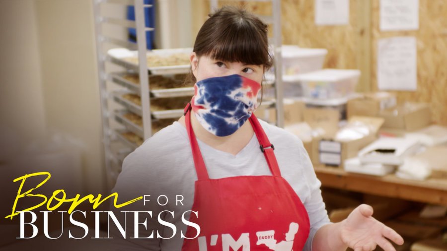 Collette Divitto in her bakery wearing a mask and apron in a scene from Born For Business. Show logo in bottom left