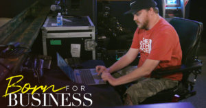 Chris working tech at a concert venue in a scene from Born For Business. Show logo in bottom left.