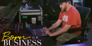 Chris working tech at a concert venue in a scene from Born For Business. Show logo in bottom left.