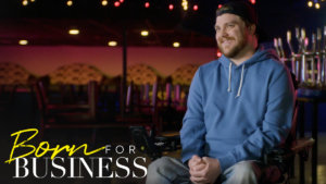 Chris in a concert venue speaking to camera in a scene from Born For Business. Show logo in bottom left