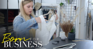 Lexi picking up a dress in a scene from Born For Business. Show logo in bottom left.