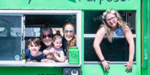 the Chernotsky family looking out the windows in a green bus, smiling