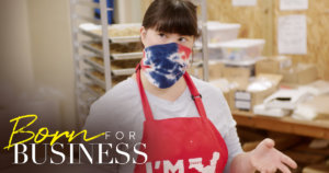 Collette Divitto in her bakery wearing a mask and apron in a scene from Born For Business. Show logo in bottom left