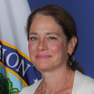 Katy Neas smiling headshot in front of a flag