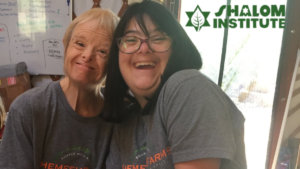 Two people with disabilities smiling wearing Shemesh Farm t-shirts. Shalom Institute logo.