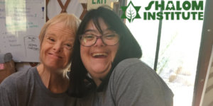 Two people with disabilities smiling wearing Shemesh Farm t-shirts. Shalom Institute logo.