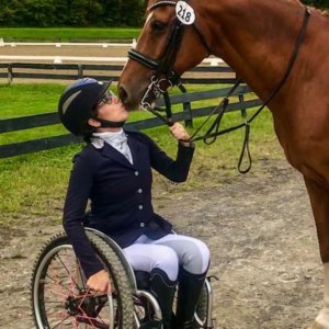 Alanna Flax-Clark with a horse kissing her face. Flax-Clark is a wheelchair user.