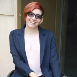 Lauren Arena smiling wearing glasses and a suit jacket. Arena is a wheelchair user.