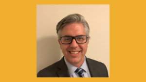 Craig Leen smiling headshot wearing glasses and a suit and tie