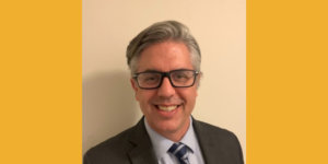 Craig Leen smiling headshot wearing glasses and a suit and tie