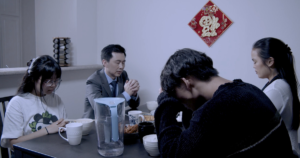 A scene from Iridescence with four people seated around a table, one with his head in his hands
