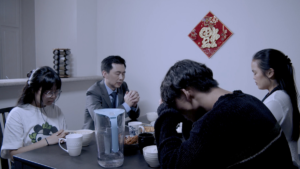 A scene from Iridescence with four people seated around a table, one with his head in his hands