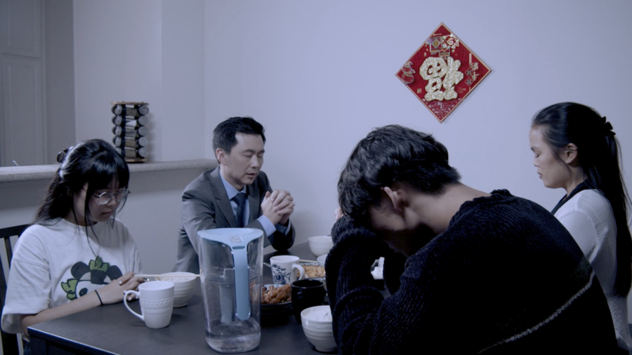 A scene from Iridescence with four people seated around a table, one with his head in his hands