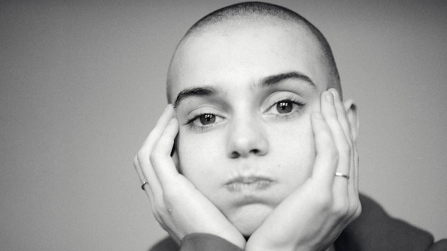 Black and white photo of Sinead O'Connor with her head in her hands.
