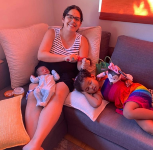 Joy St. Juste smiling seated on a couch with her children lying down with her.