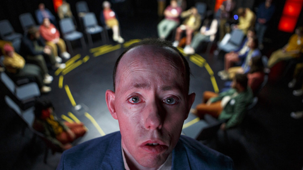 A still from Shadow with one of the main characters looking at the camera in a meeting room