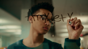 A scene from "Just Like You" with a teenager writing the word "anxiety" in marker on glass