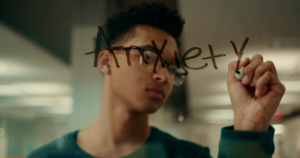 A scene from "Just Like You" with a teenager writing the word "anxiety" in marker on glass