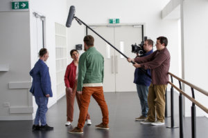 A behind-the-scenes photo from the set of Shadow with the three main characters talking with a boom mic over their heads