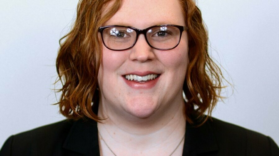 Ariel Simms smiling headshot wearing glasses and a blazer