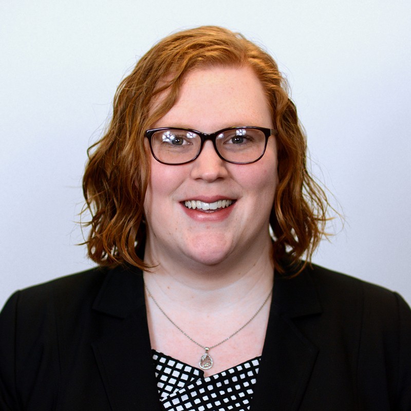 Ariel Simms smiling headshot wearing glasses and a blazer