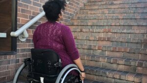 An African American woman in a wheelchair looking up a flight of stairs