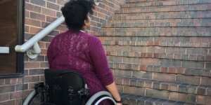 An African American woman in a wheelchair looking up a flight of stairs