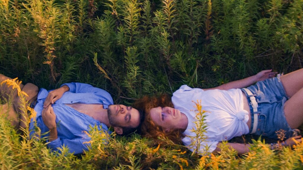 Two characters from Unidentified Objects lying in the grass with their heads touching each other