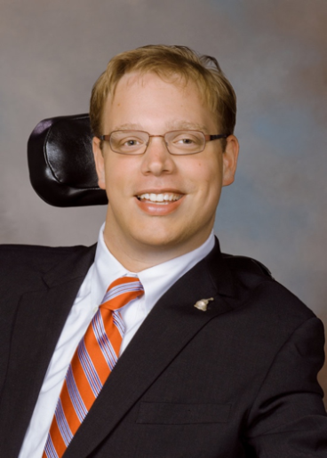 Matthew Shapiro headshot wearing a suit and tie and seated in his wheelchair