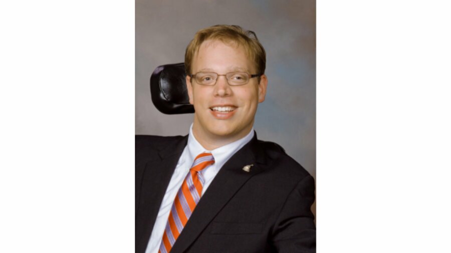 Matthew Shapiro headshot wearing a suit and tie and seated in his wheelchair