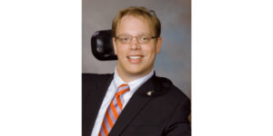 Matthew Shapiro headshot wearing a suit and tie and seated in his wheelchair