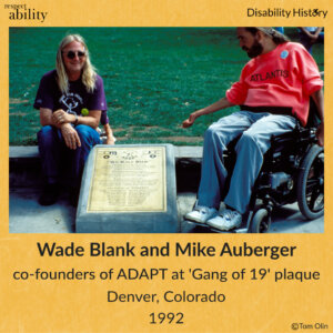 photo of Wade Blank and Mike Auberger next to Gang of 19 plaque on the side walk with ADAPT logo and ‘We will ride” visible. Text: Wade Blank and Mike Auberger. co-founders of ADAPT at 'Gang of 19' plaque. Denver, Colorado. 1992. Source: Tom Olin