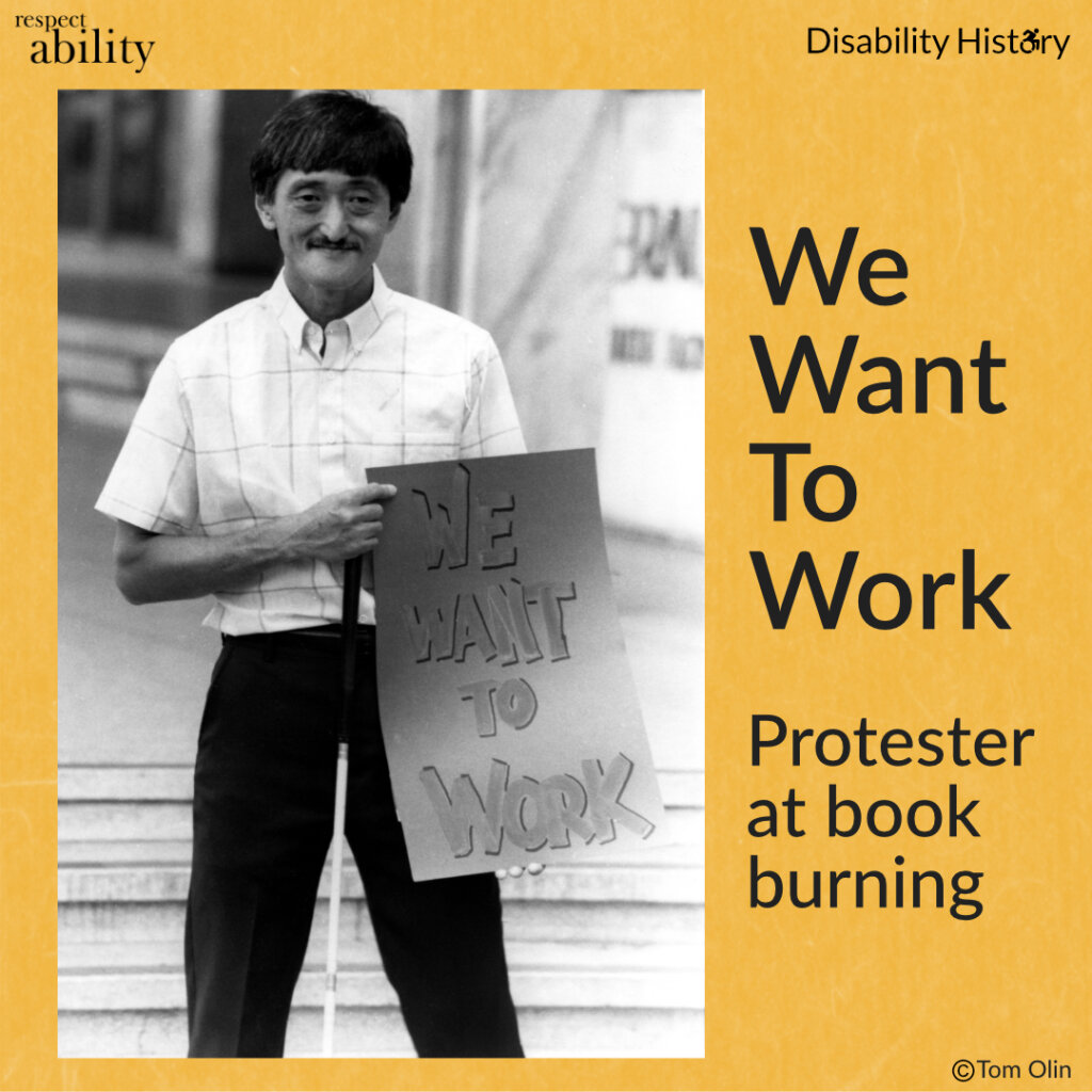 Black and white photo of man with a mustache smiling while holding his guide cane and showing a sign that says, “We Want to Work.” Text: We Want To Work. Protester at book burning. Source: Tom Olin.