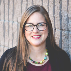 Jasmine Duckworth smiling headshot wearing glasses in front of a stone wall