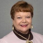 Sharon Gomez smiling headshot with gold earrings and a gold necklace