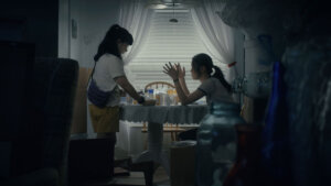 Jeena Yi and Anna Sargent in Take Me Home at a dinner table having an animated conversation