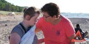 A scene from "Teacher of Patience" with Emily and a woman talking on a beach. Slamdance logo in bottom right corner.