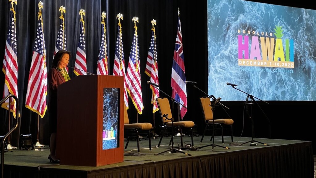 Hawaii Lt. Governor Sylvia Luke speaking at the 2022 CSG National Conference in Hawaii in front of American flags and the conference's logo on the screen behind her