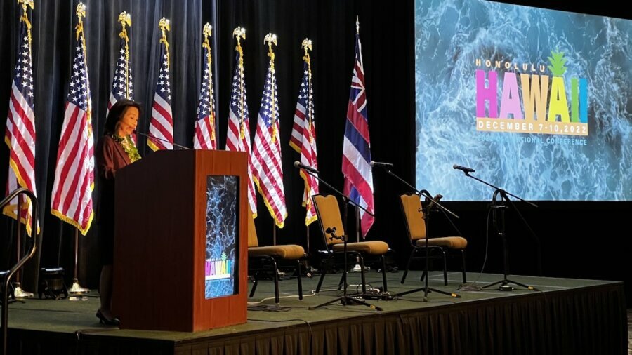Hawaii Lt. Governor Sylvia Luke speaking at the 2022 CSG National Conference in Hawaii in front of American flags and the conference's logo on the screen behind her