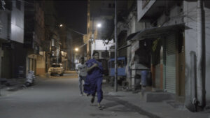 A scene from Aleeya with Aleeya running down a street with a man running after her